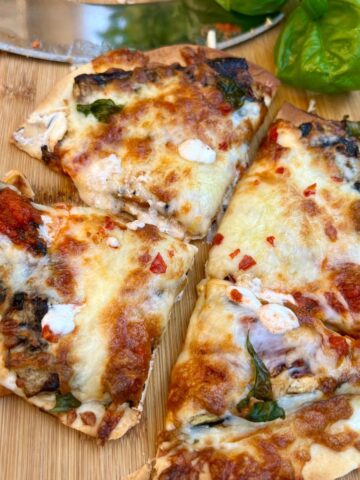 Low carb air fryer tortilla pizza on a wood cutting board with a chopper and fresh basil
