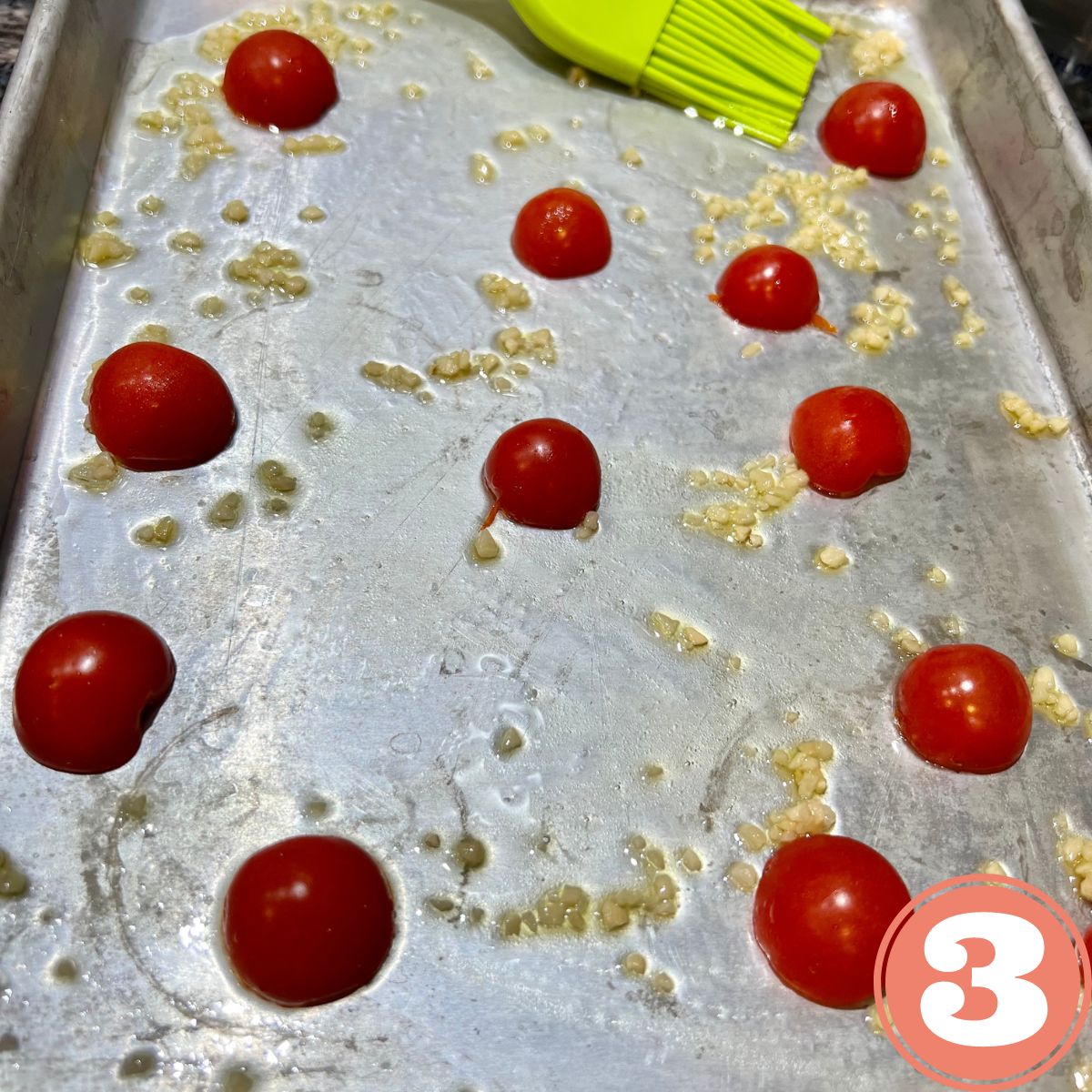 sheet pan with grape tomatoes olive oil and crushed garlic being mixed with a green brush