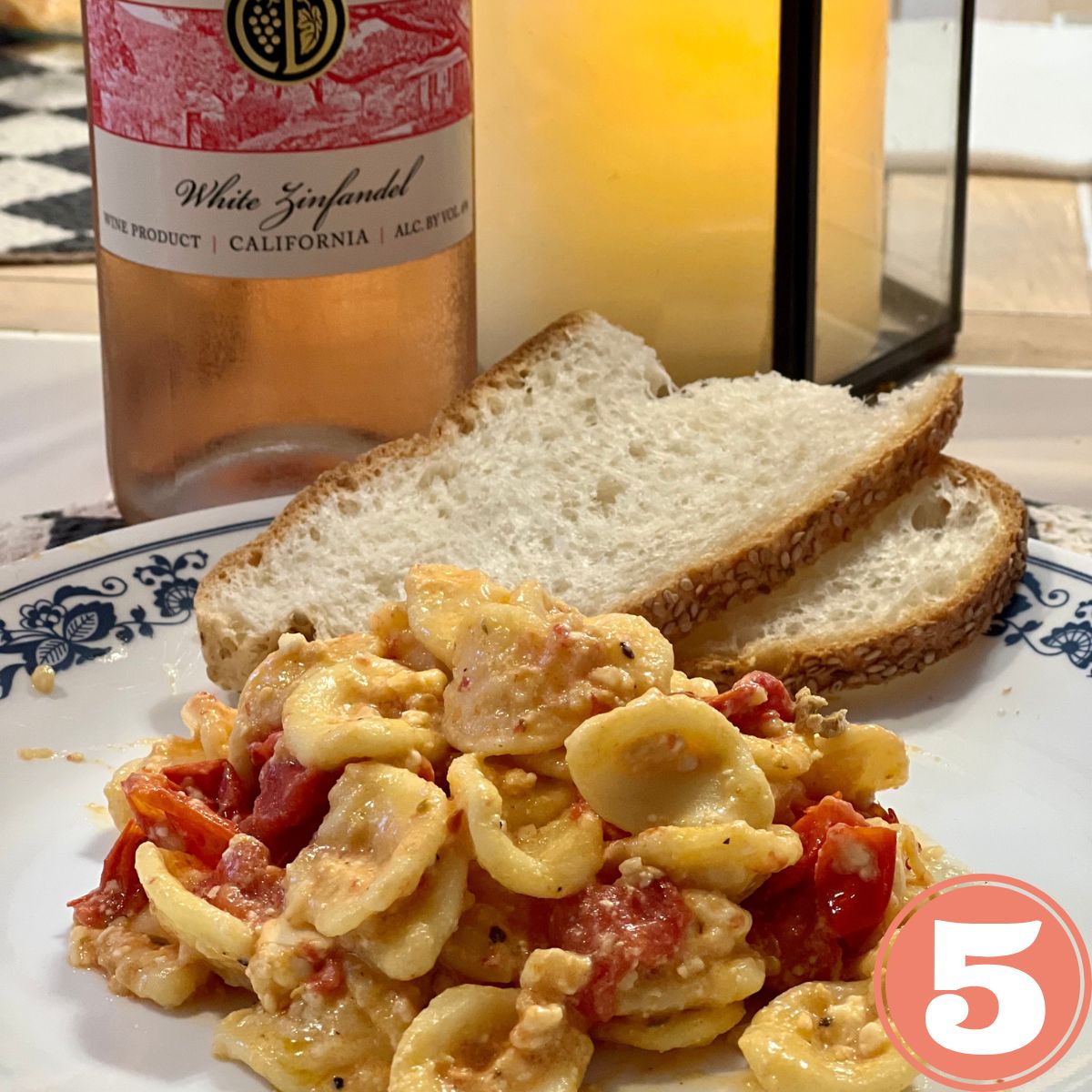 Easy feta cheese tomato pasta salad on a white dish with sliced Italian bread and a bottle of white wine