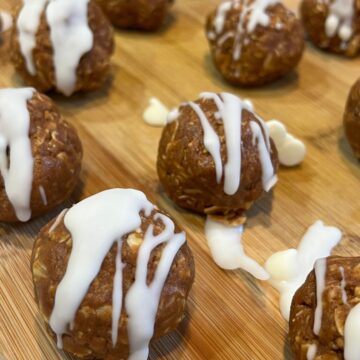Pumpkin spice energy balls drizzled with white chocolate on a wooden cutting board