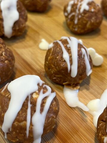 Pumpkin spice energy balls drizzled with white chocolate on a wooden cutting board