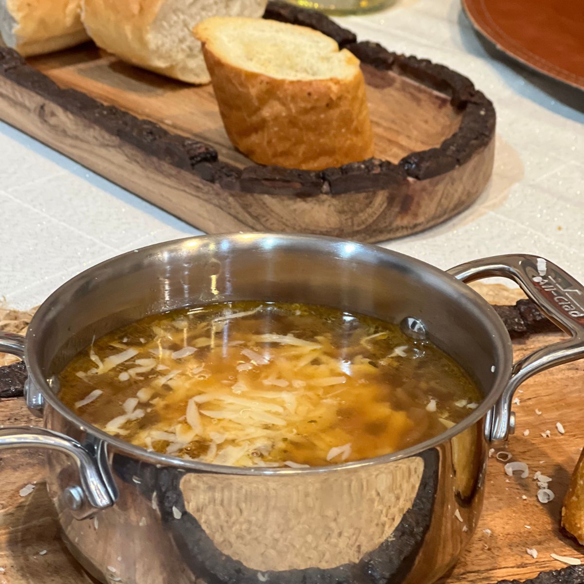 Crockpot French onion soup in a stainless steel pot with sliced bread on the side