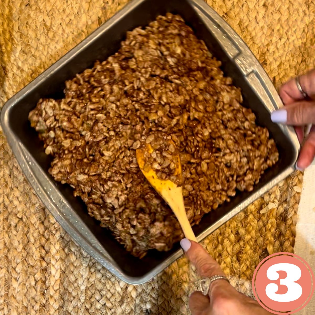 A wooden spoon flattening Rice Krispies in a baking pan