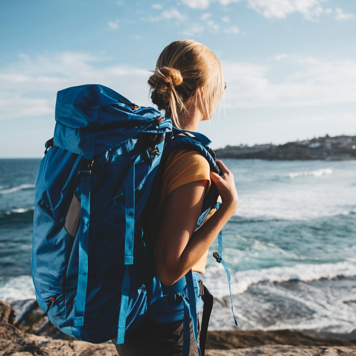 blonde female wearing a blue backpack by the water