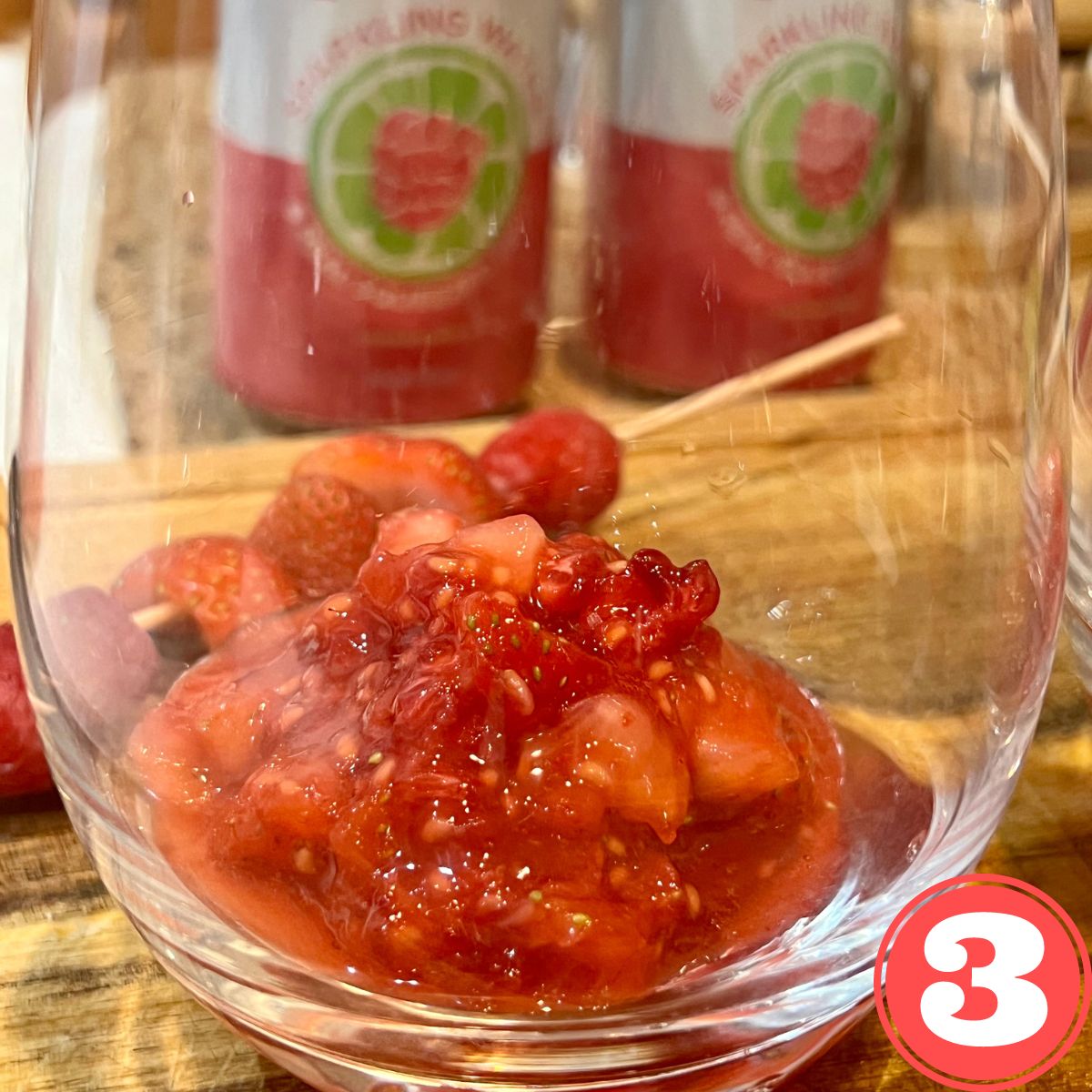 A wine glass with smashed strawberries and raspberries on the bottom