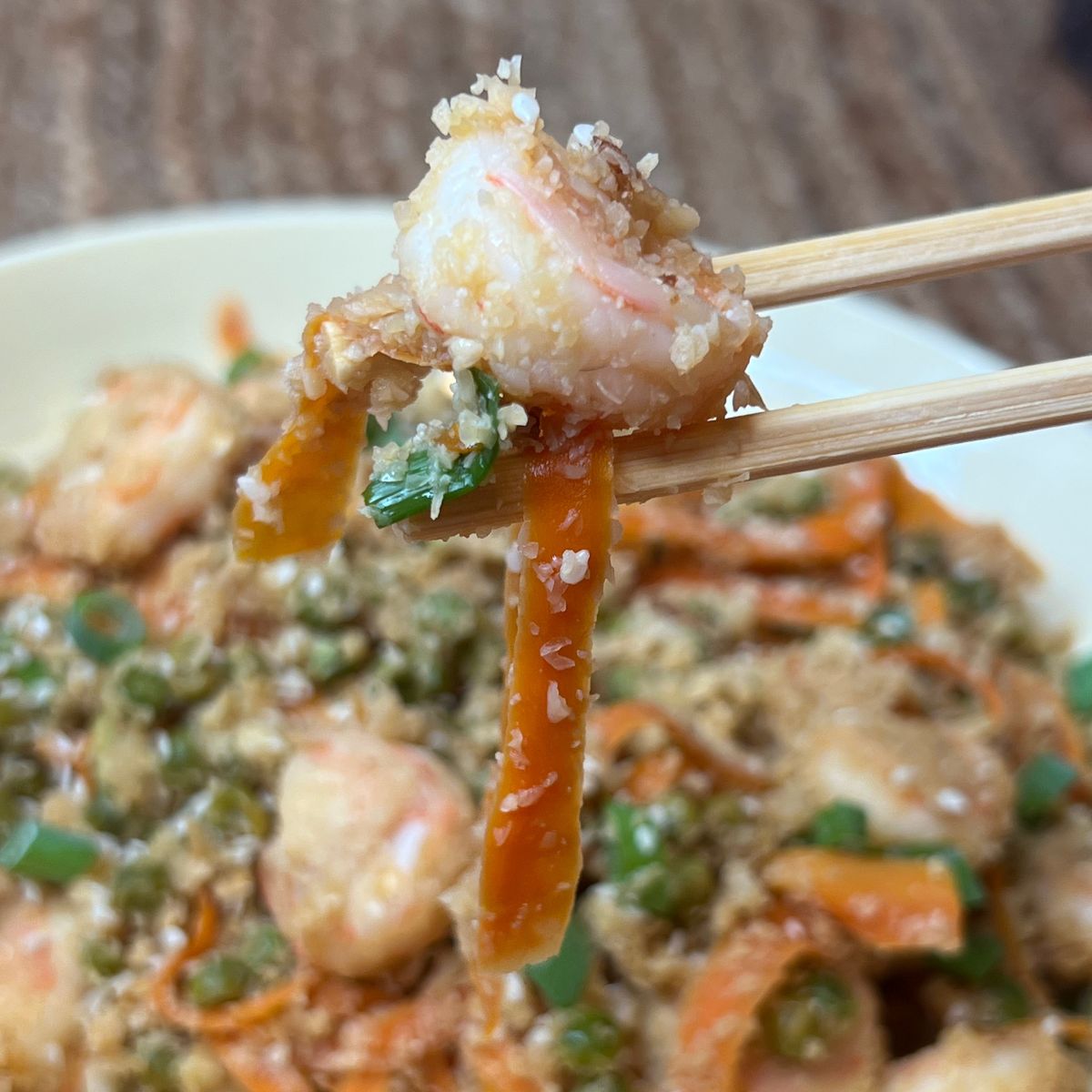 One shrimp being picked up with chopsticks over a bowl of cauliflower fried rice