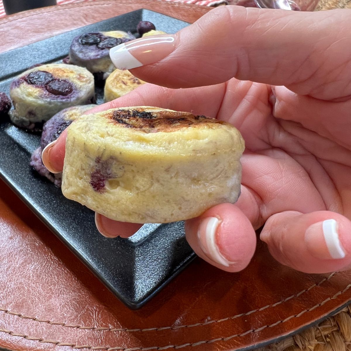 A hand holding a mini blueberry pancake bite