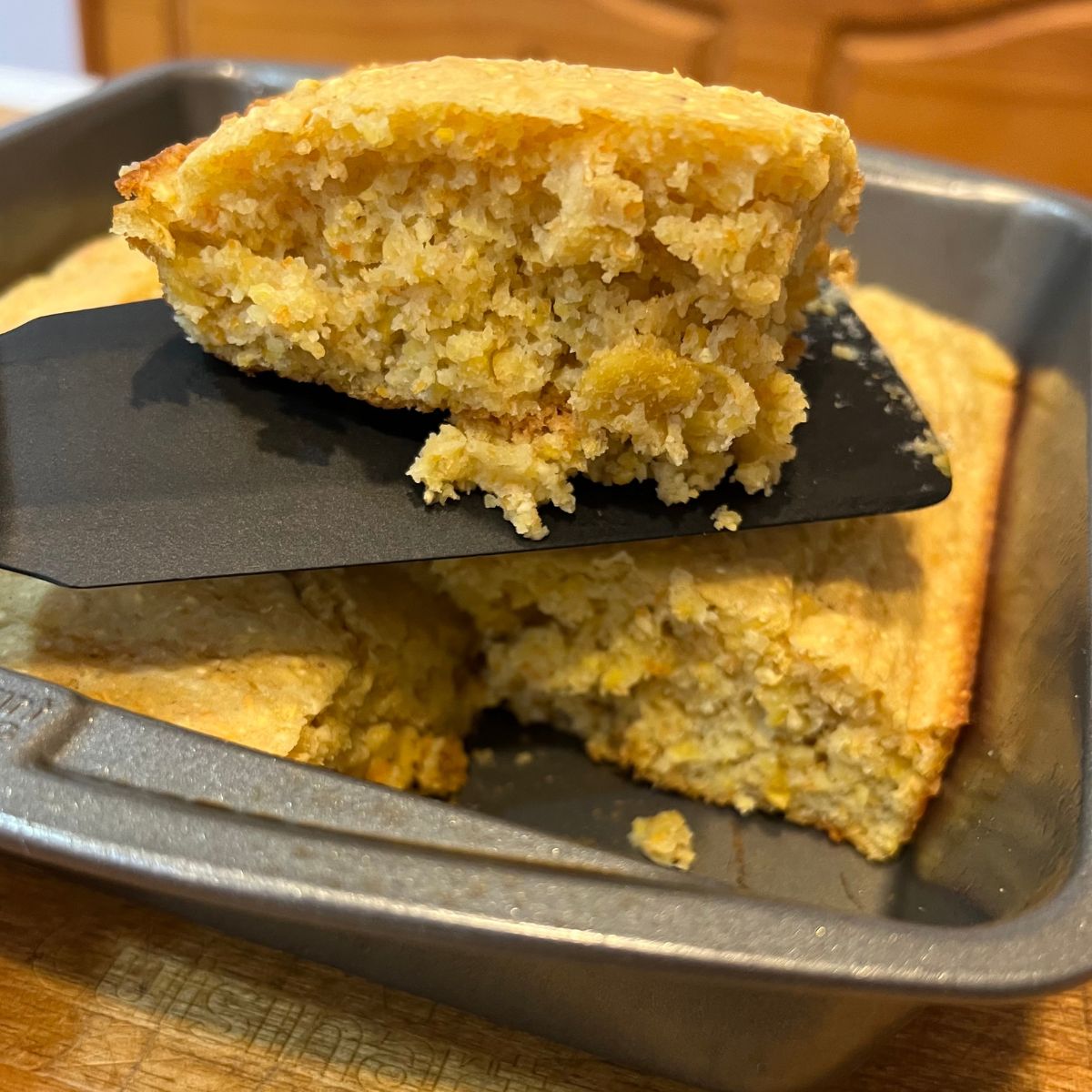 A slice of WW cornbread on a black spatula over a tray of cornbread