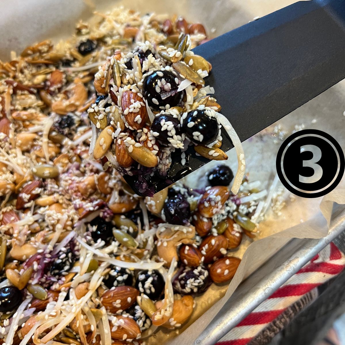 Blueberry nut keto granola on a spatula over a tray of homemade granola