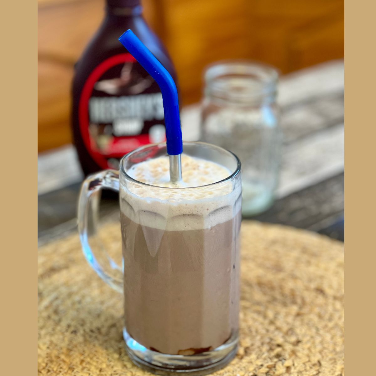 A chocolate egg cream in a glass beer mug with a blue straw in it on a table