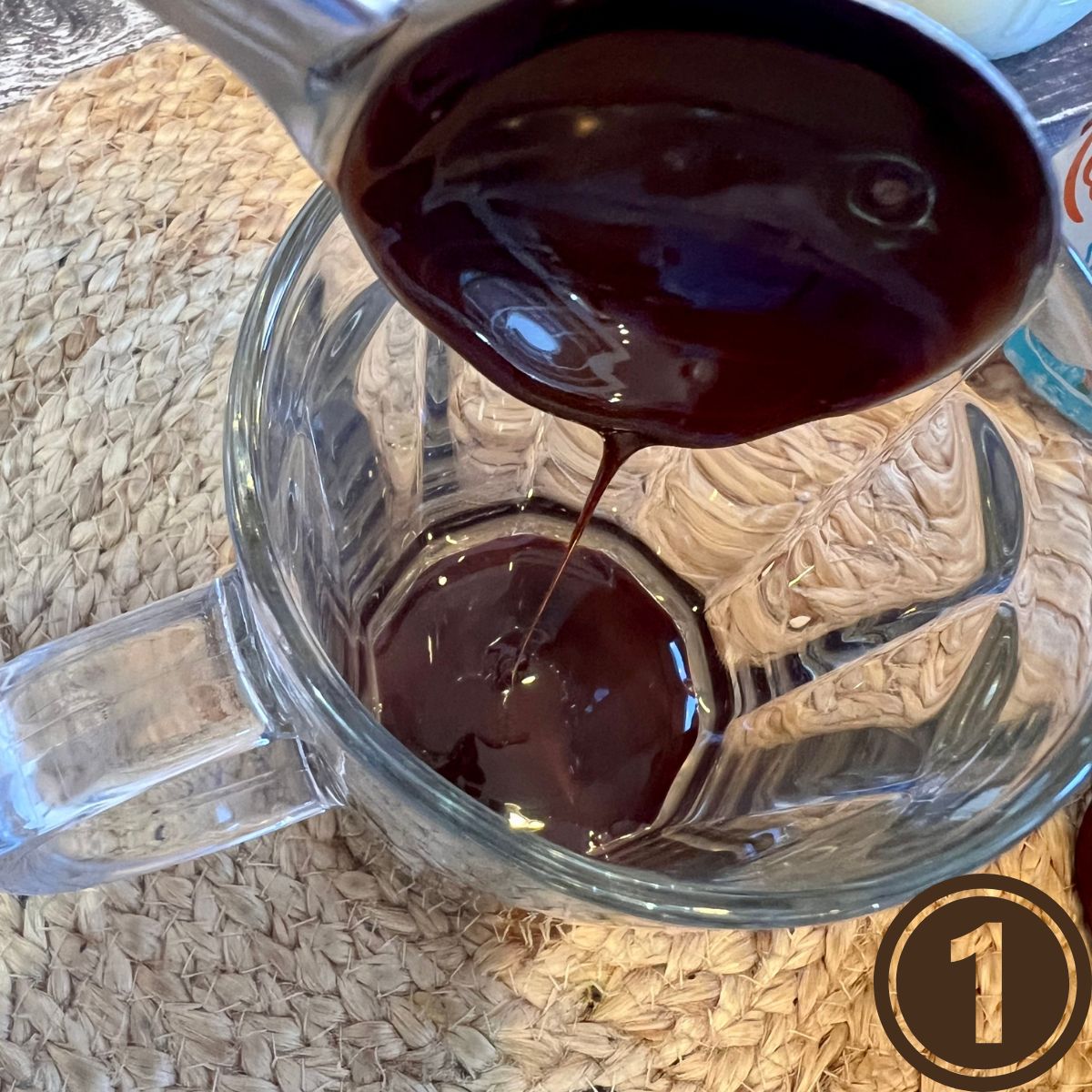 A spoon pouring chocolate syrup into a glass