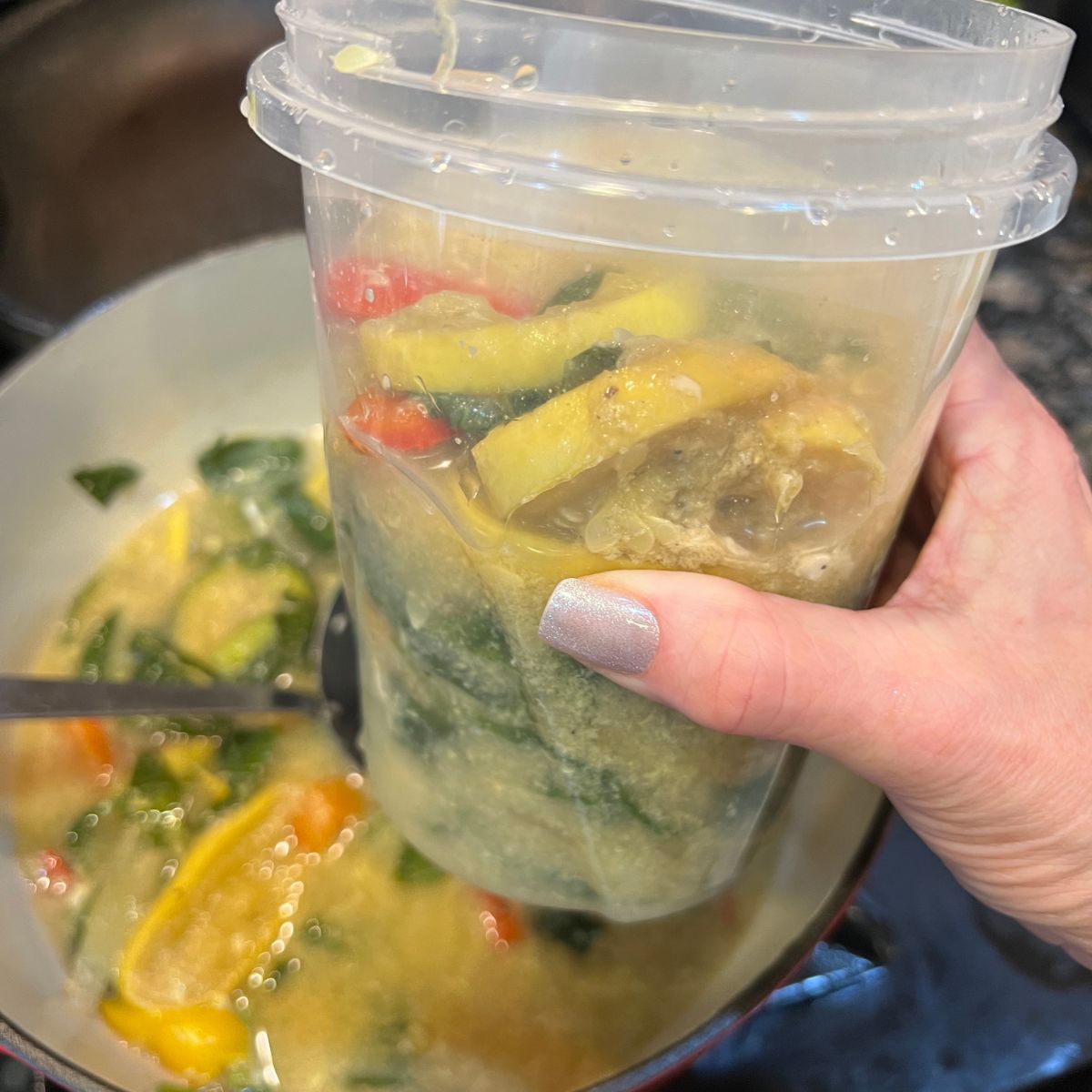 A hand holding a container of yellow squash soup