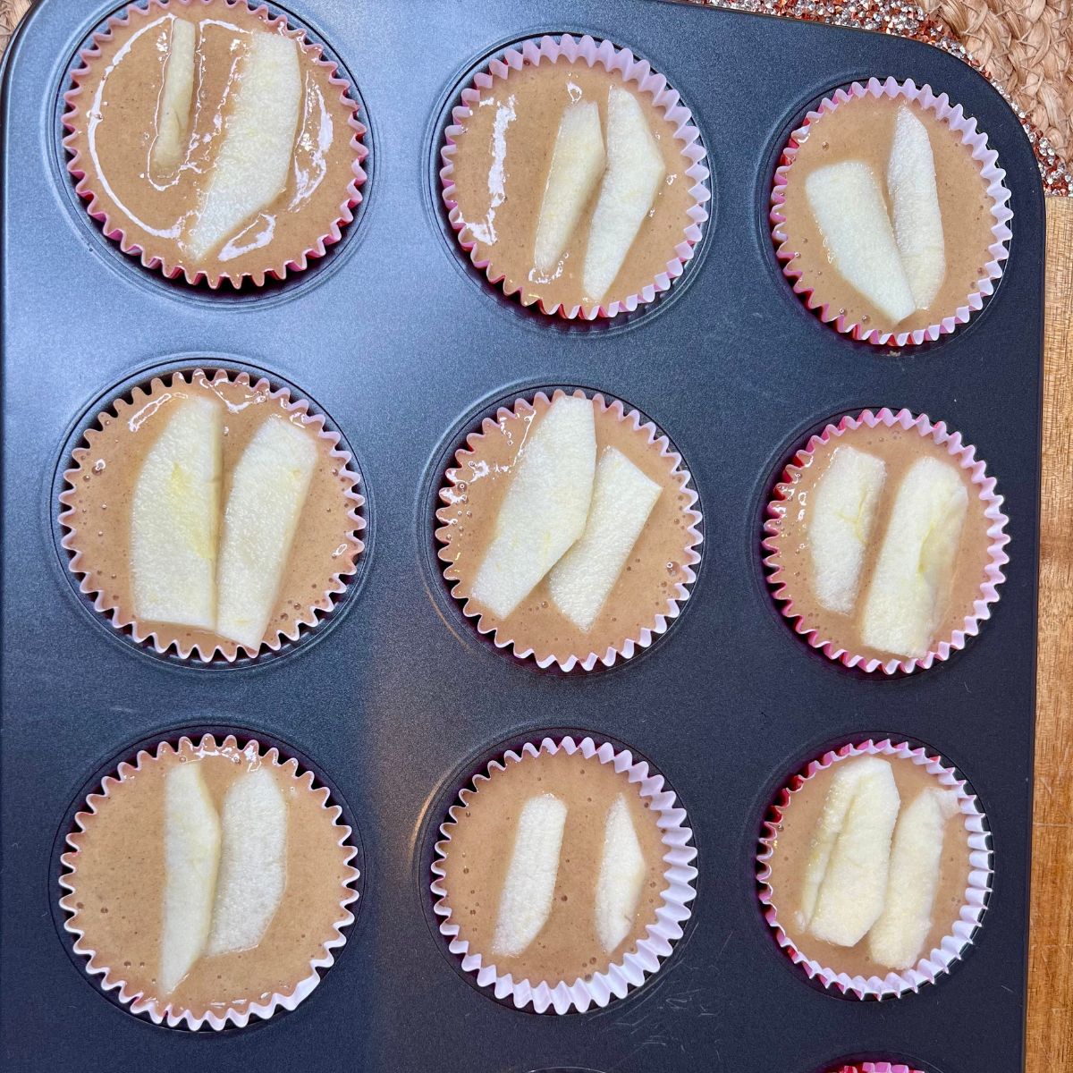 Muffin batter with apple slices on top in a muffin tin