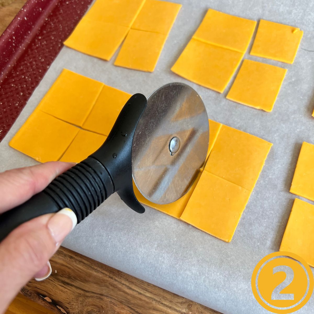 A pizza cutter slicing cheese squares into four squares