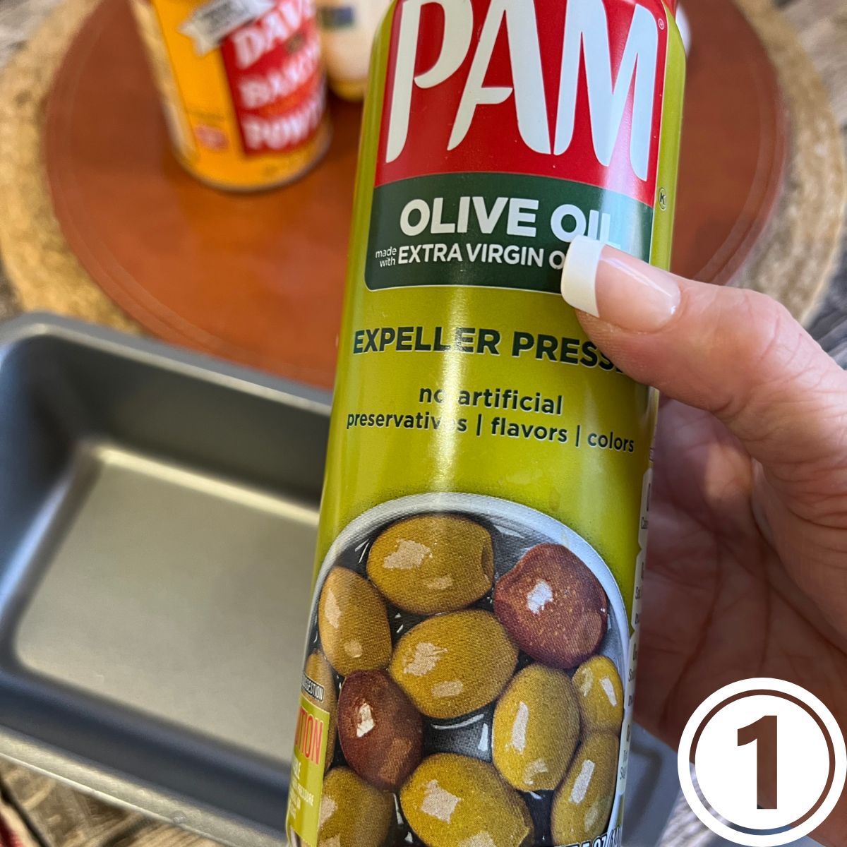 A hand holding a can of spray olive oil