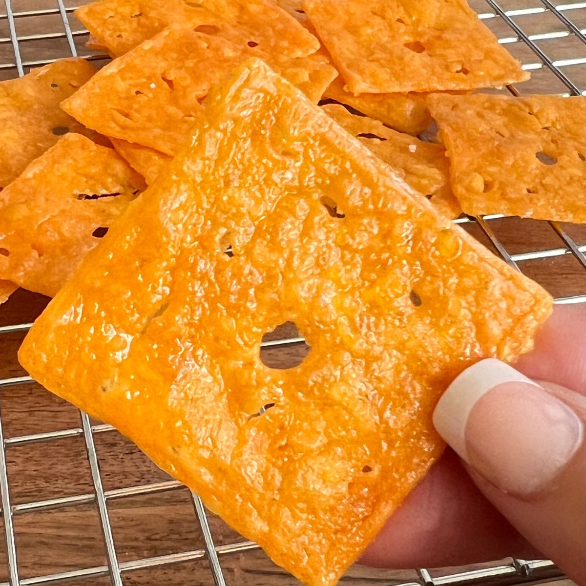 A hand holding one homemade keto Cheezit