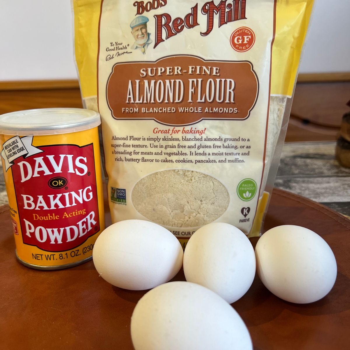 4 eggs, a bag of almond flour and a jar of baking powder on a table