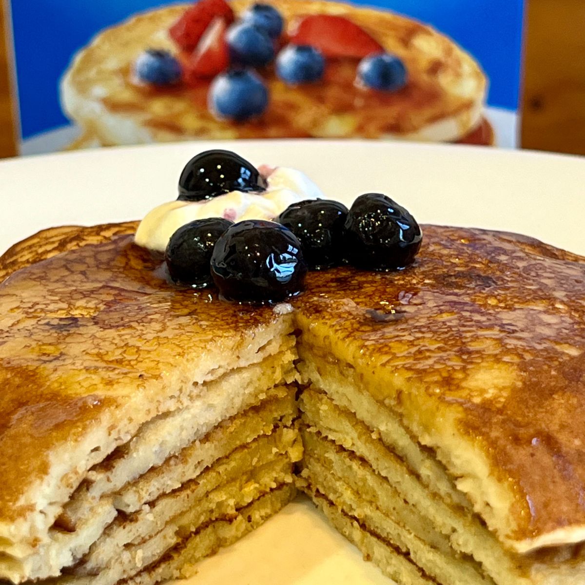A stack of Krusteaz Buttermilk pancakes with blueberries and whipped cream on top
