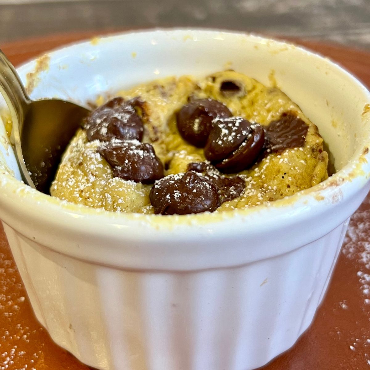 A protein powder mug cake with chocolate chips on top in a white ramekin