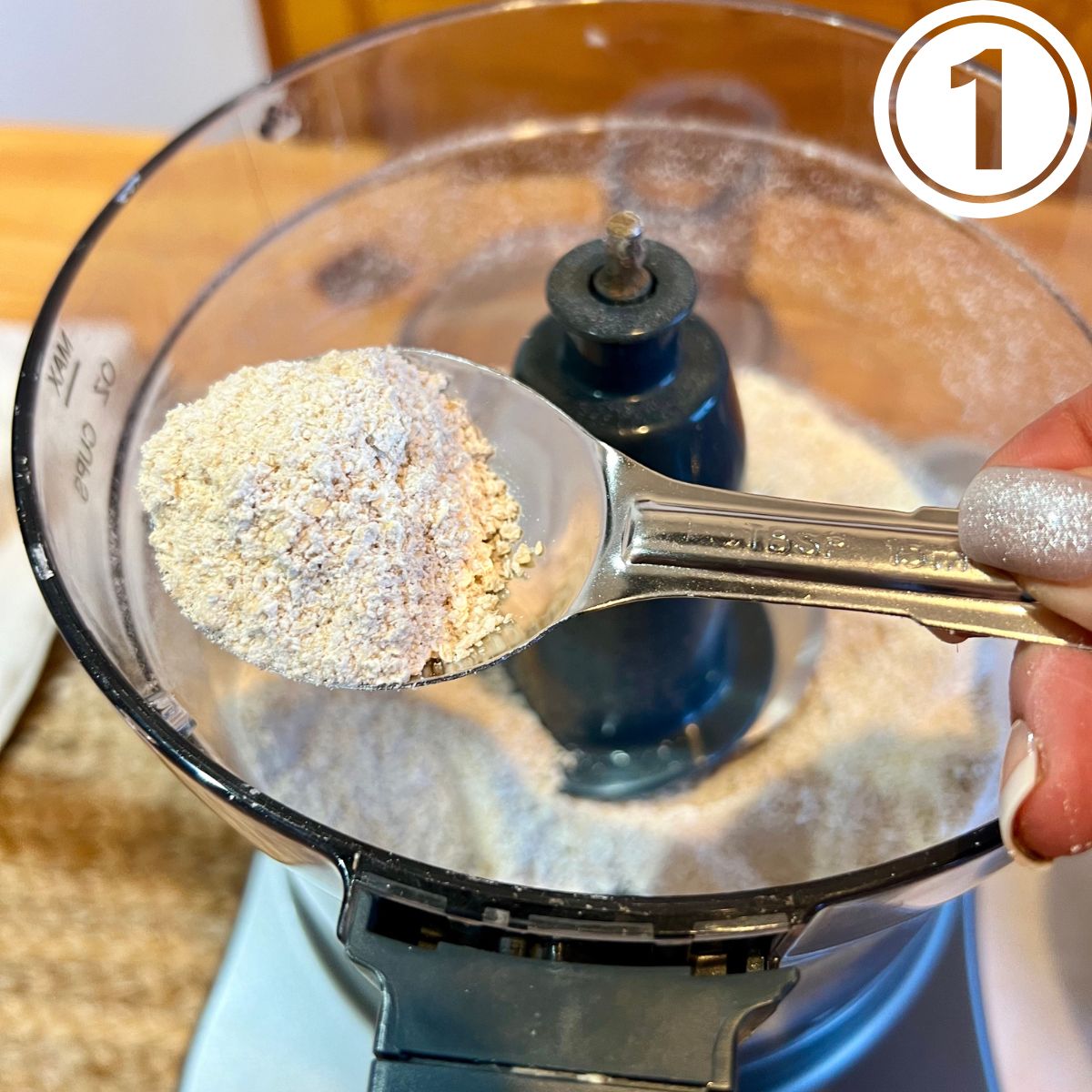 A spoon holding rolled oats fine flour over a food processor