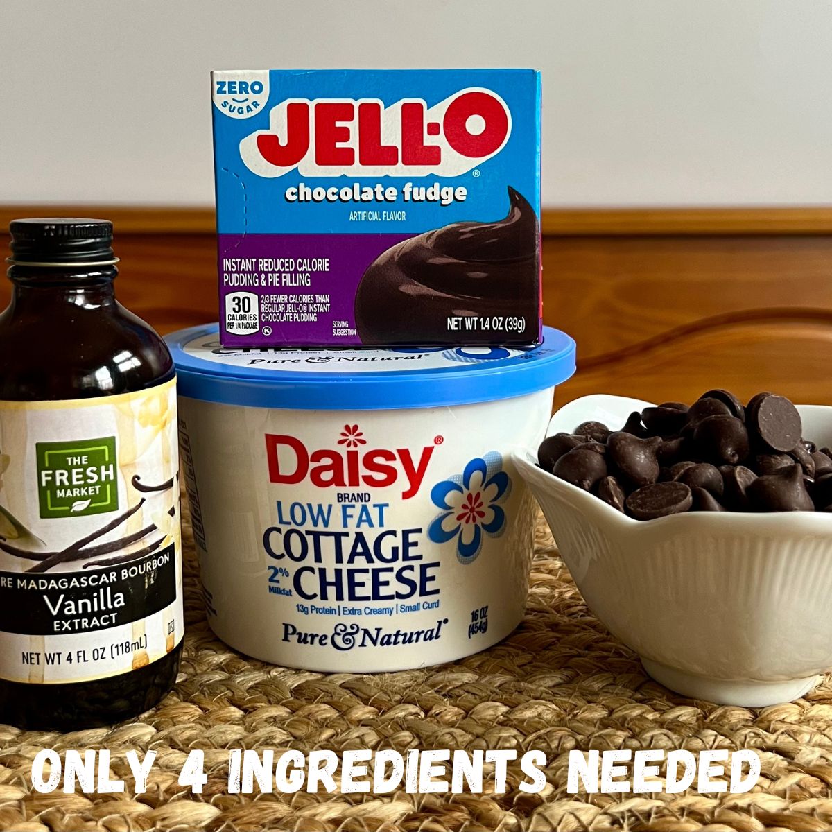 A bottle of vanilla extract, a container of cottage cheese, a box of chocolate jello instant pudding and a bowl of chocolate chips