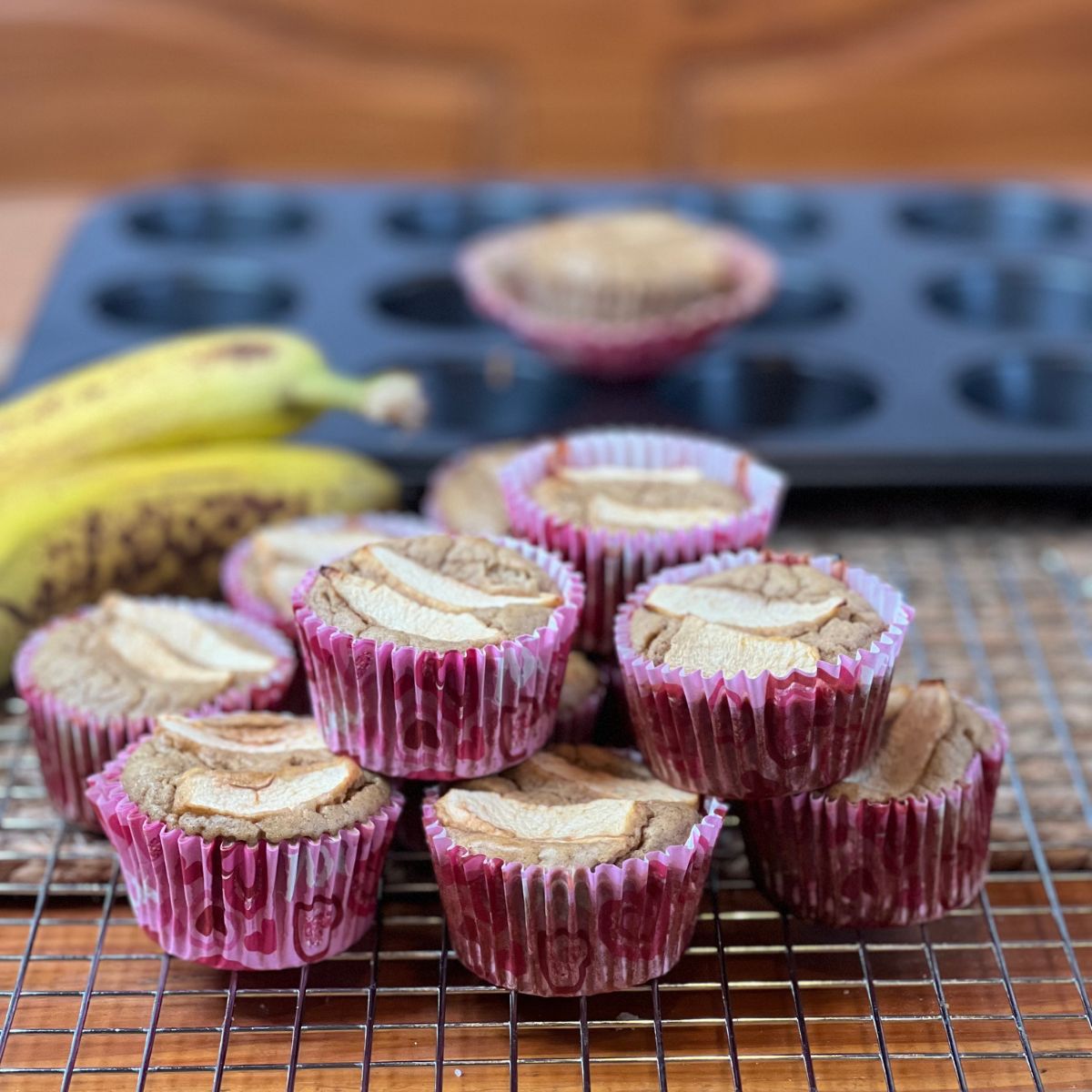 A stack of Weight Watchers Banana Bread Muffins on a table with two bananas and a muffin tin