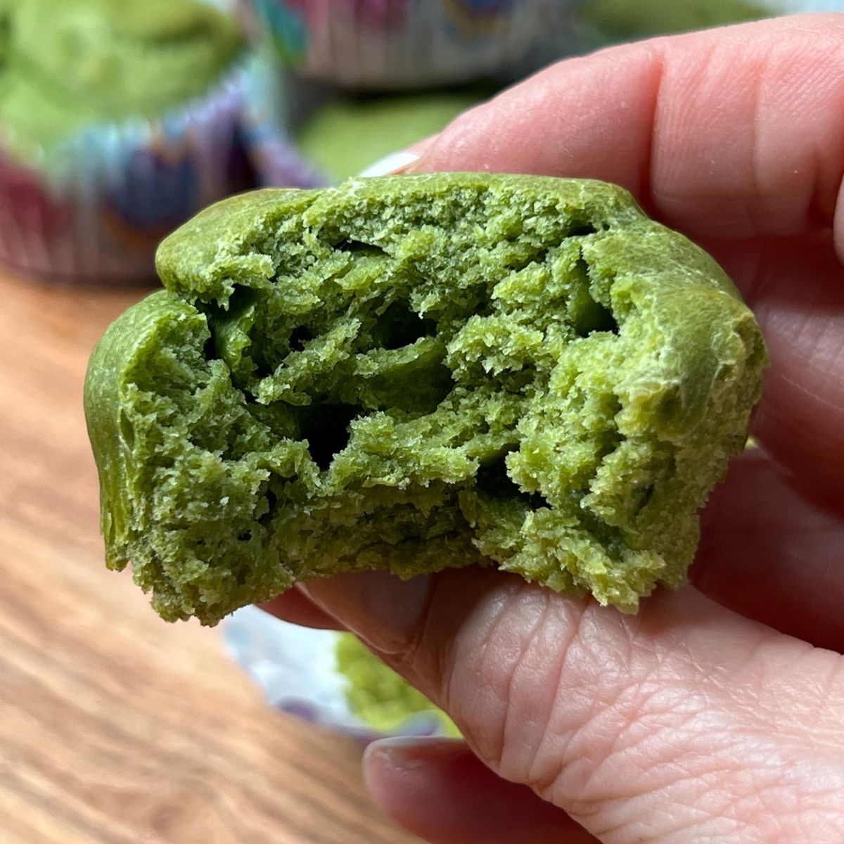 A hand holding a banana spinach muffin with a bite taken out of it