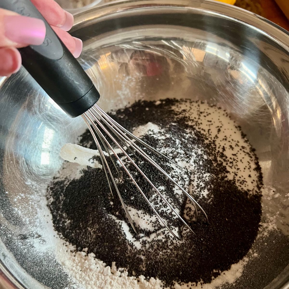 A whisk in a bowl with flour and poppy seeds