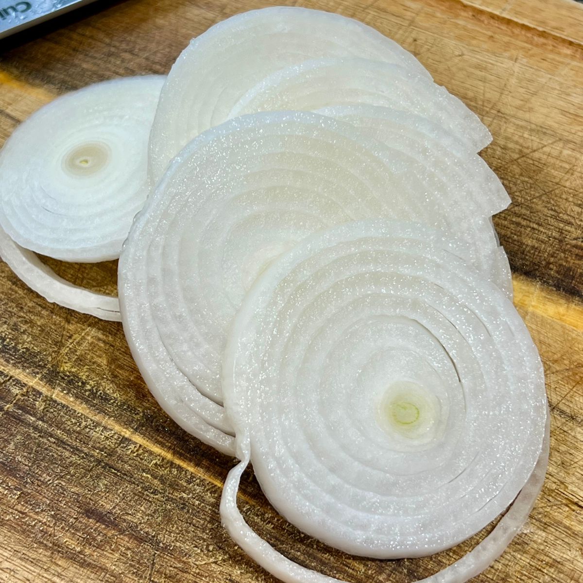 Sliced white onion rings on a wooden cutting board