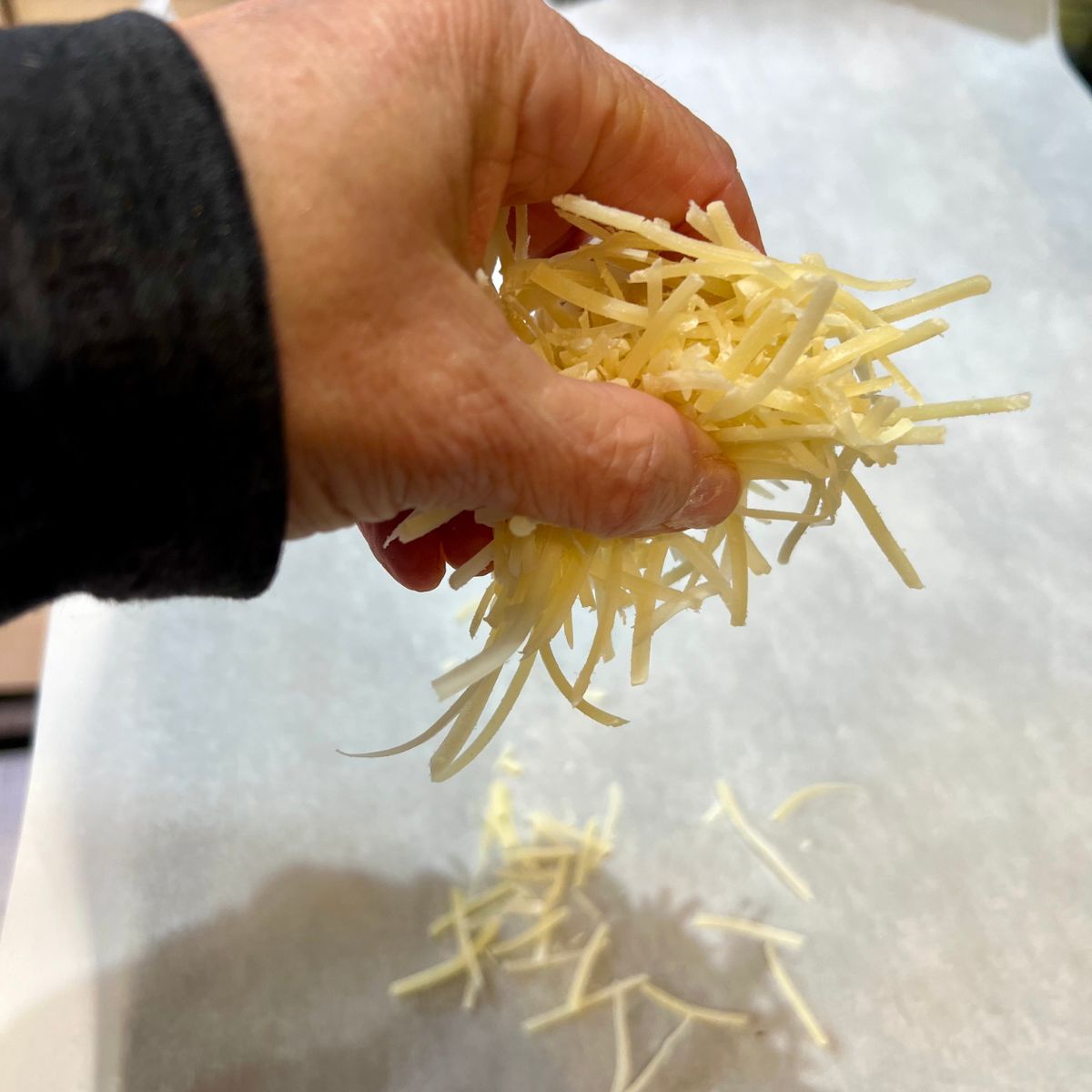 a hand holding shredded parmesan cheese over a sheet pan