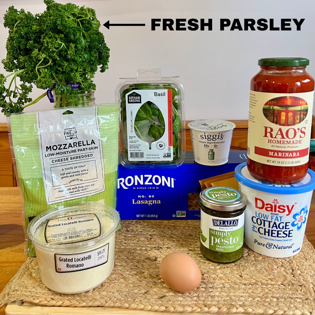 Parsley, basil, marinara sauce, lasagna noodles, pesto, egg, grated cheese and mozzarella on a table