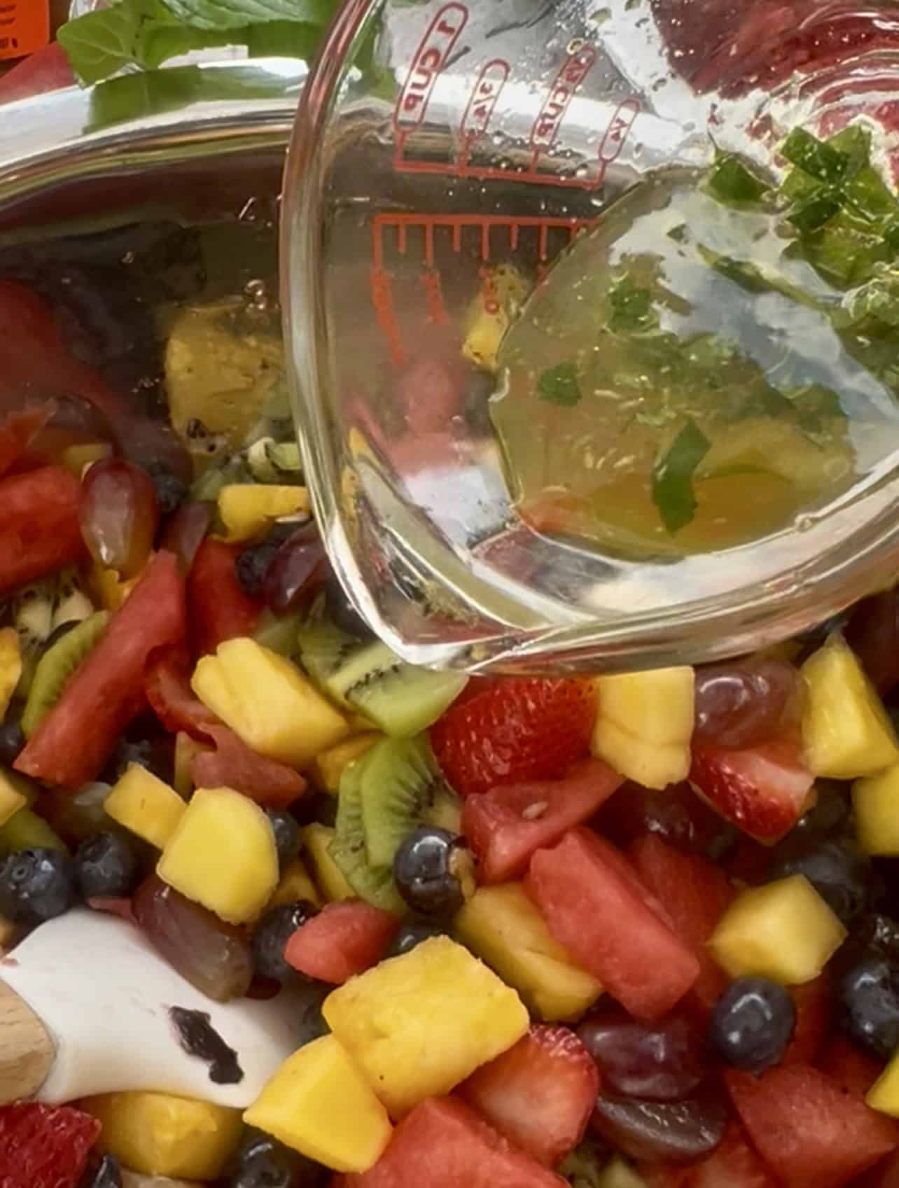 Lime-mint-honey dressing being poured over a summer fruit salad