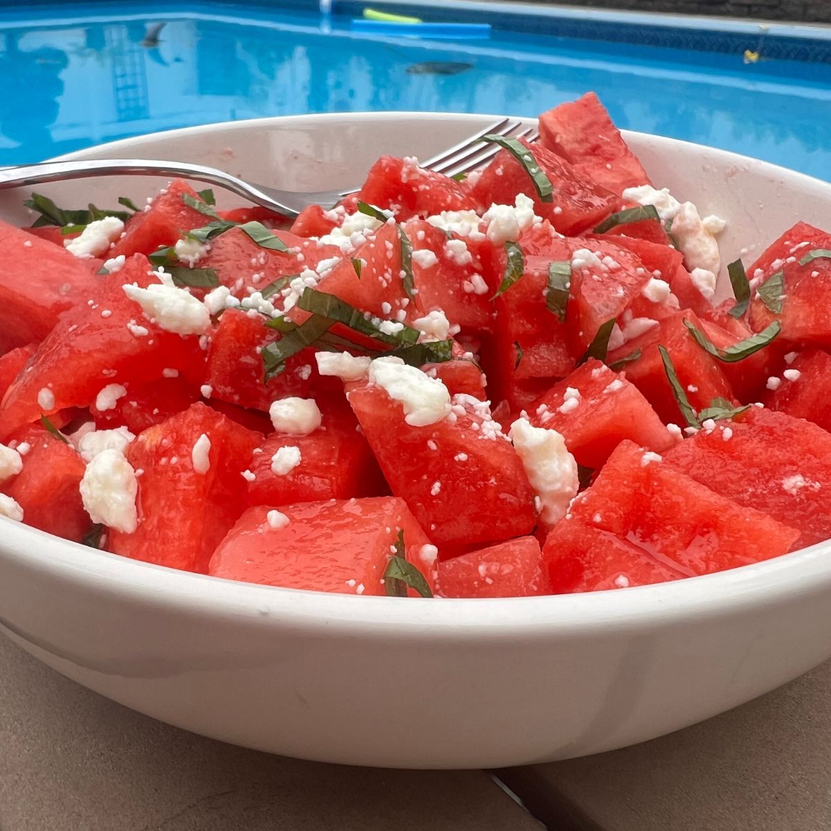 Watermelon salad with feta cheese and mint in a white bowl by the pool