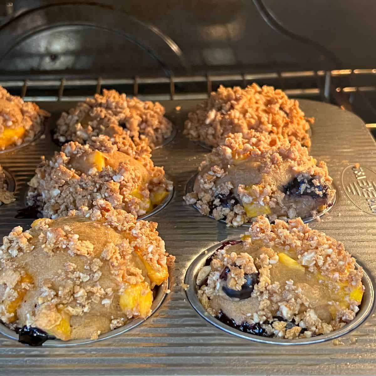 Healthy peach blueberry muffins with graham cracker topping baking in an oven
