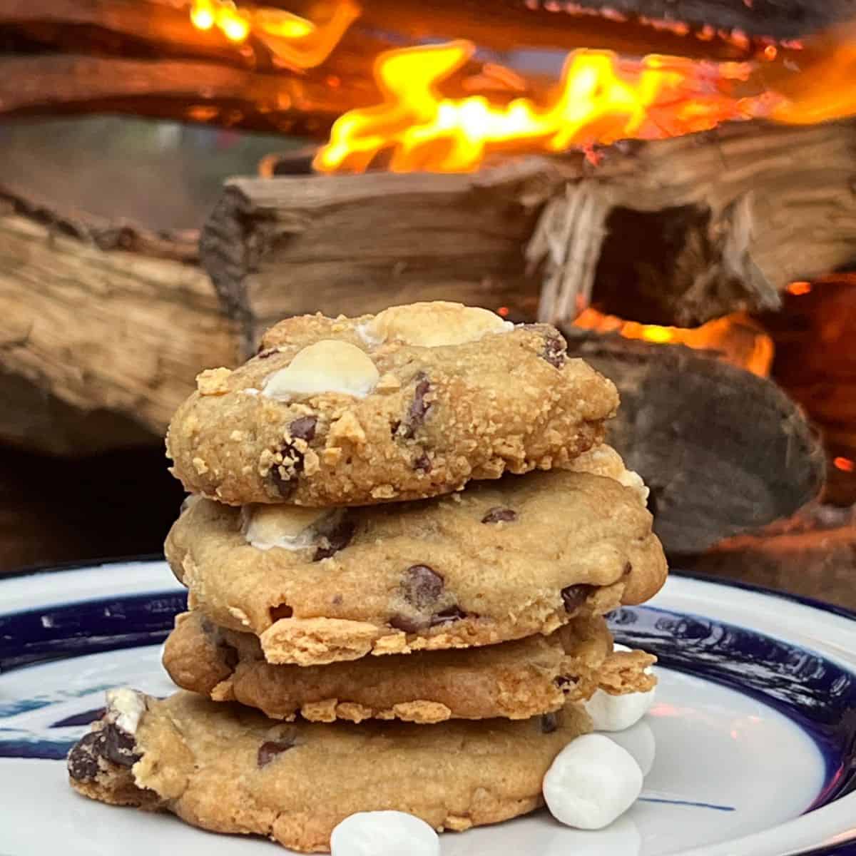Campfire S'mores Chocolate chip cookies stacked on a plate next to a fire