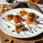Dark chocolate drizzled pistachio mandarin oranges on a white plate