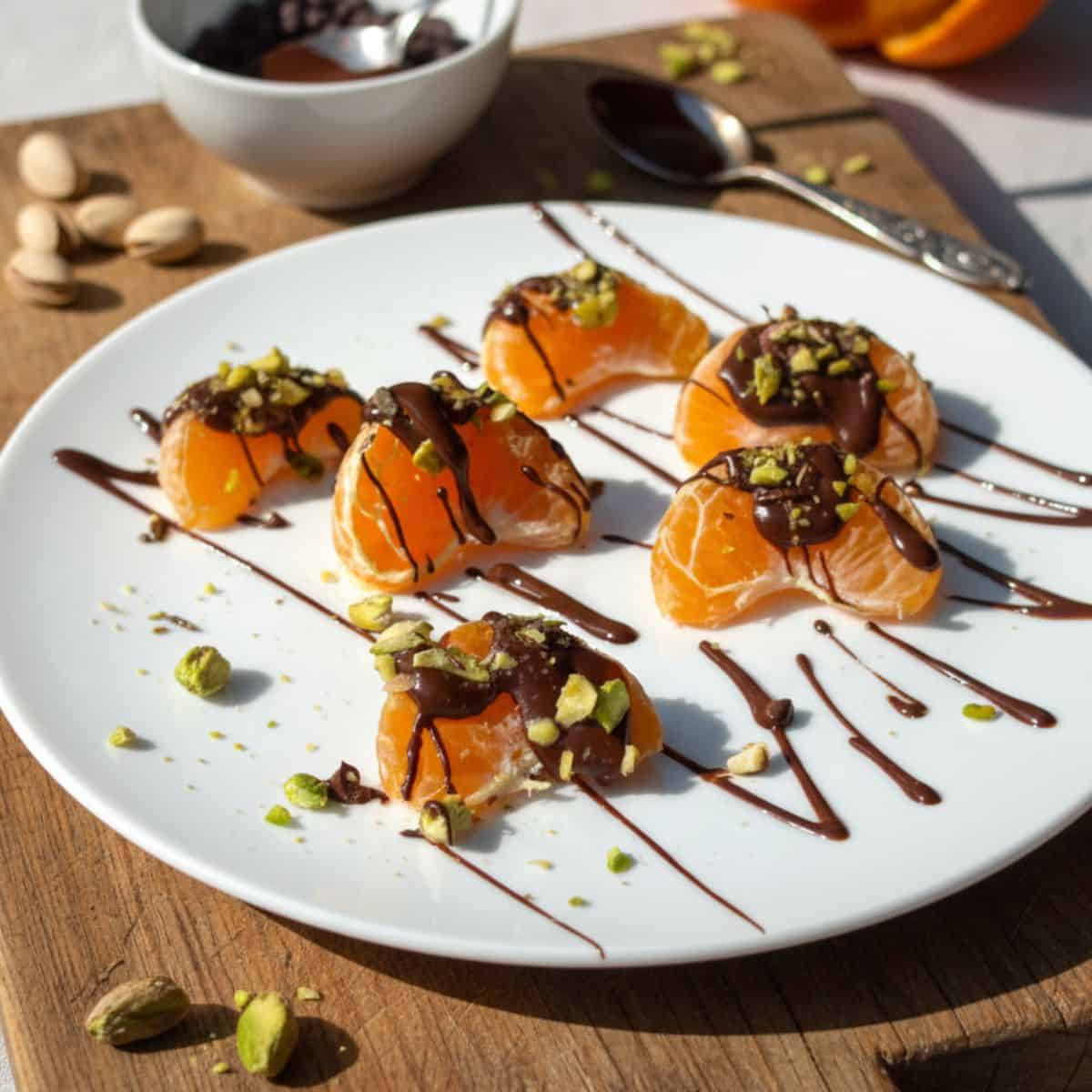 Dark chocolate drizzled pistachio mandarin oranges on a white plate