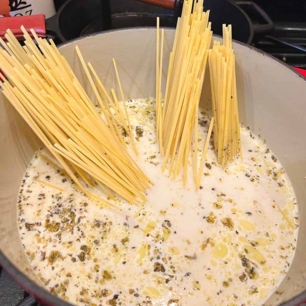 Uncooked pasta in a stockpot with creamy garlic sauce