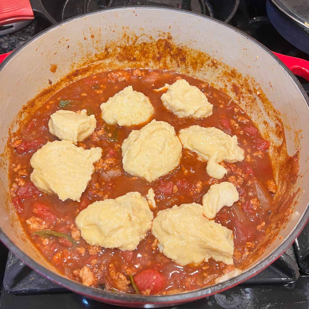 spoonfuls of Jiffy Muffin batter on top of chicken chili in a dutch oven