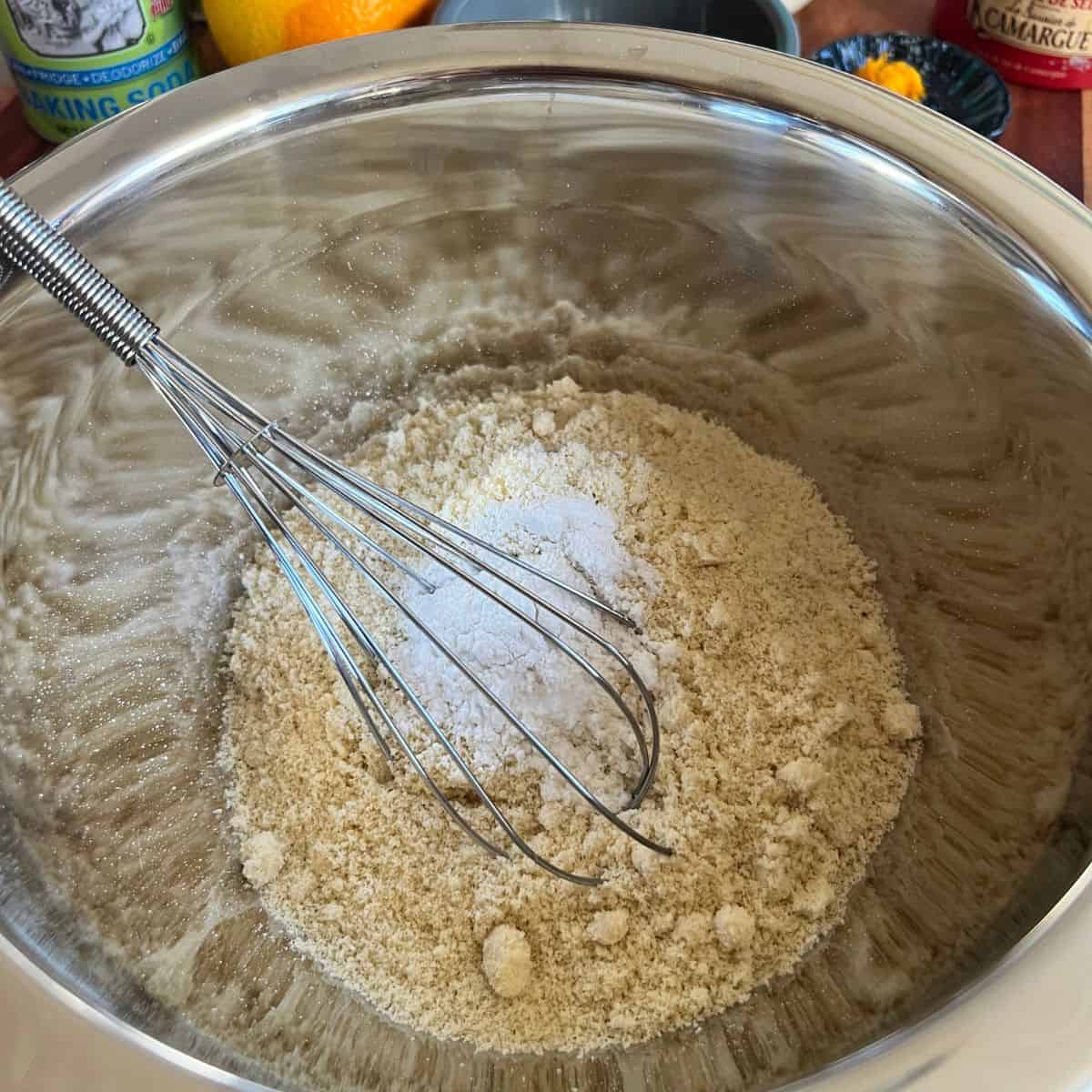 Oat flour and almond flour in a bowl with a whisk for cranberry-orange muffin recipe