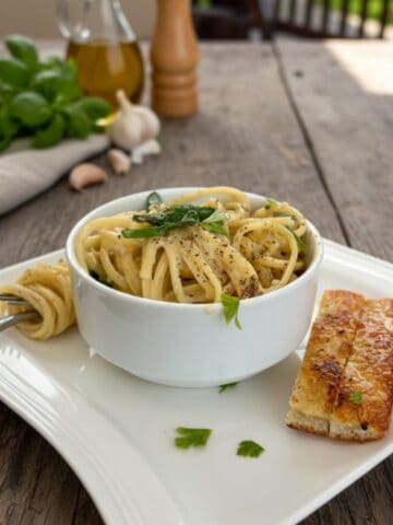 Lightend up one-pot creamy garlic pasta in a white bowl on a wooden table with breadsticks