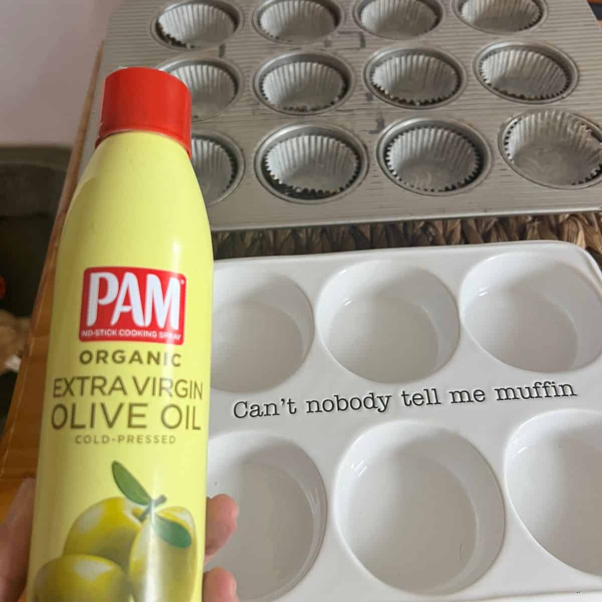 A ceramic muffin pan and aluminum muffin pan with a can of olive oil spray