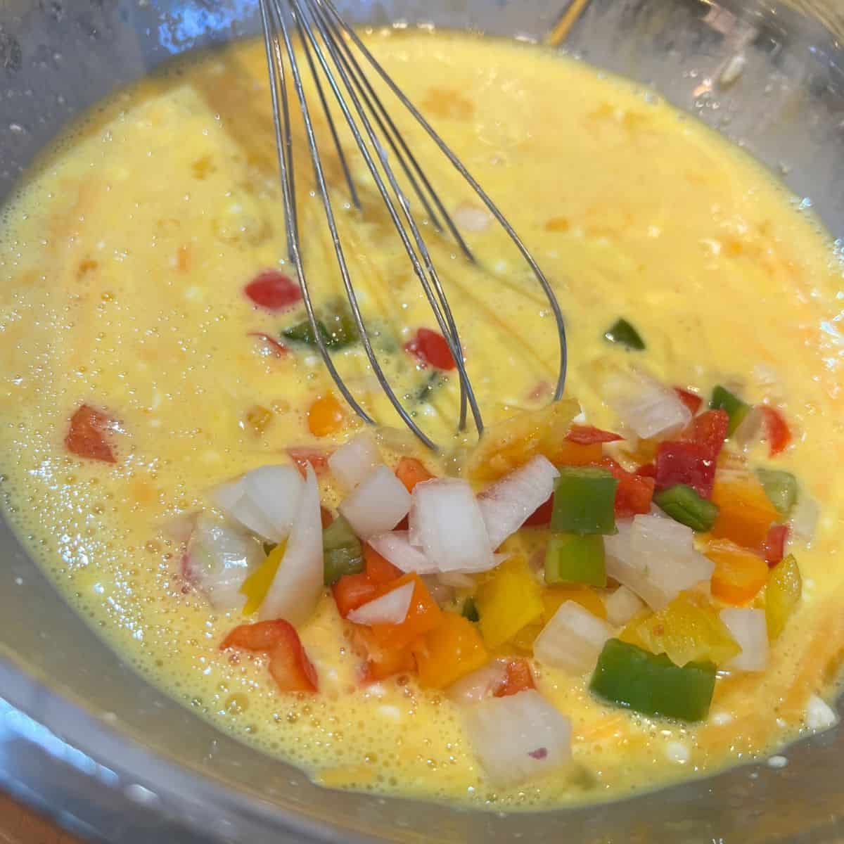 Diced onions and peppers in a bowl with eggs for high protein egg muffins