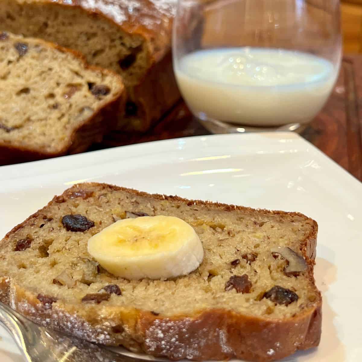 A slice of high protein cottage cheese banana bread with a slice of banana on top and a glass of milk
