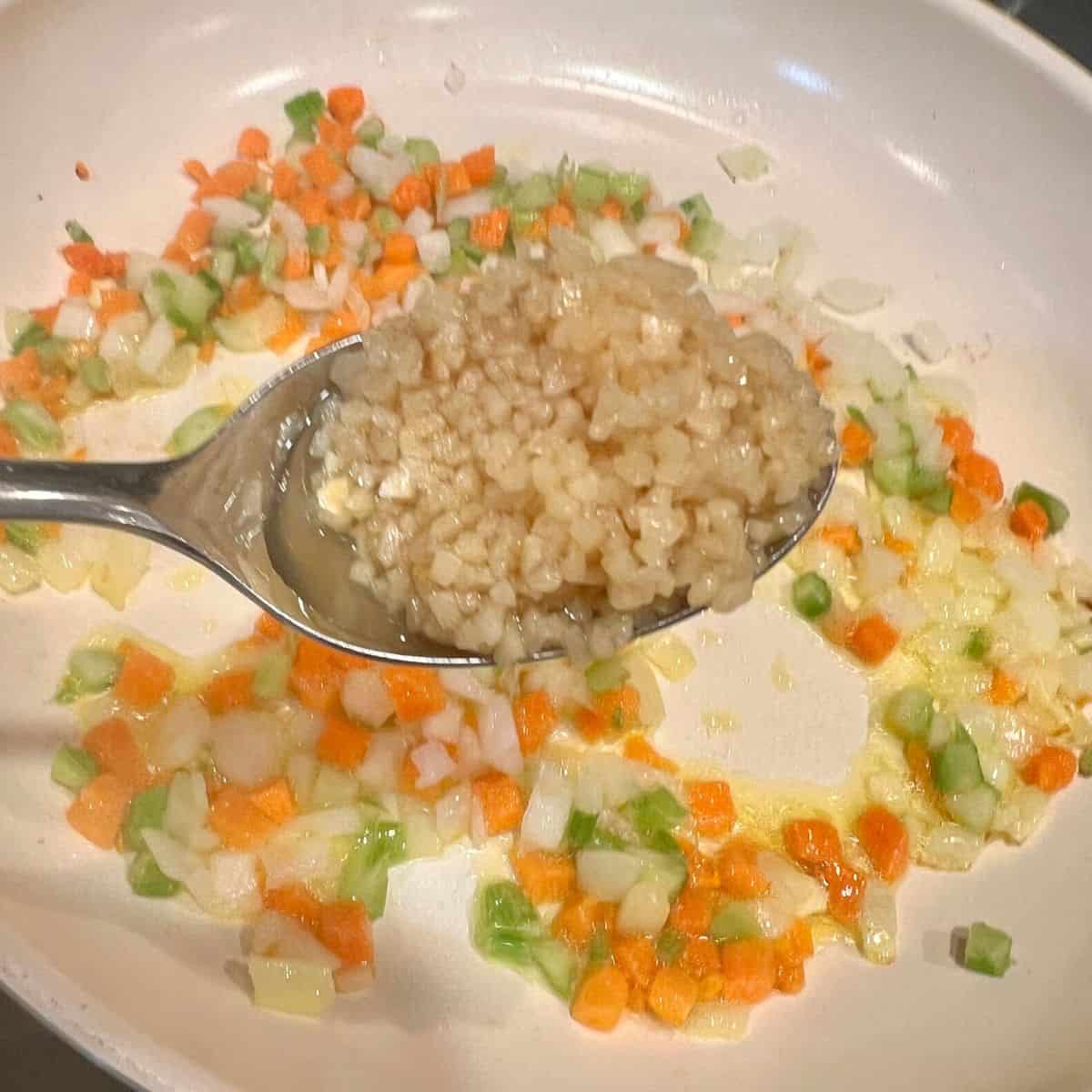 A spoonful full of garlic over pan of diced veggies for sheet pan tacos