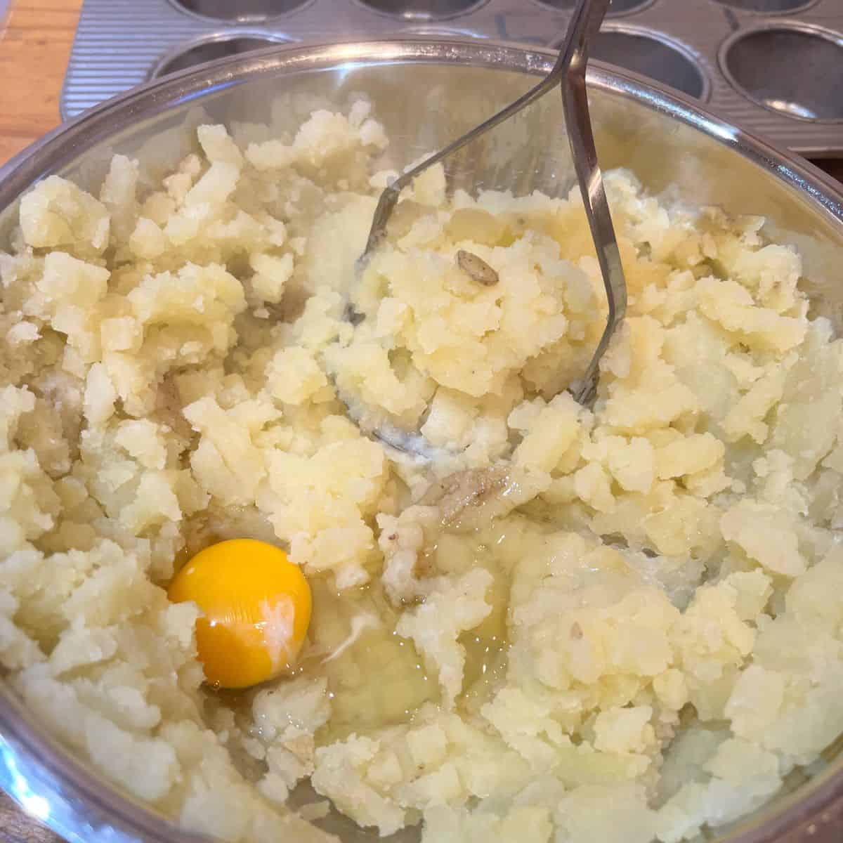 Mashing potatoes with a potato masher in a stainless steel bowl