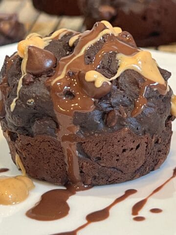 Close-up of healthy chocolate chip peanut butter muffin with melted chocolate and peanut butter drizzle on a white plate