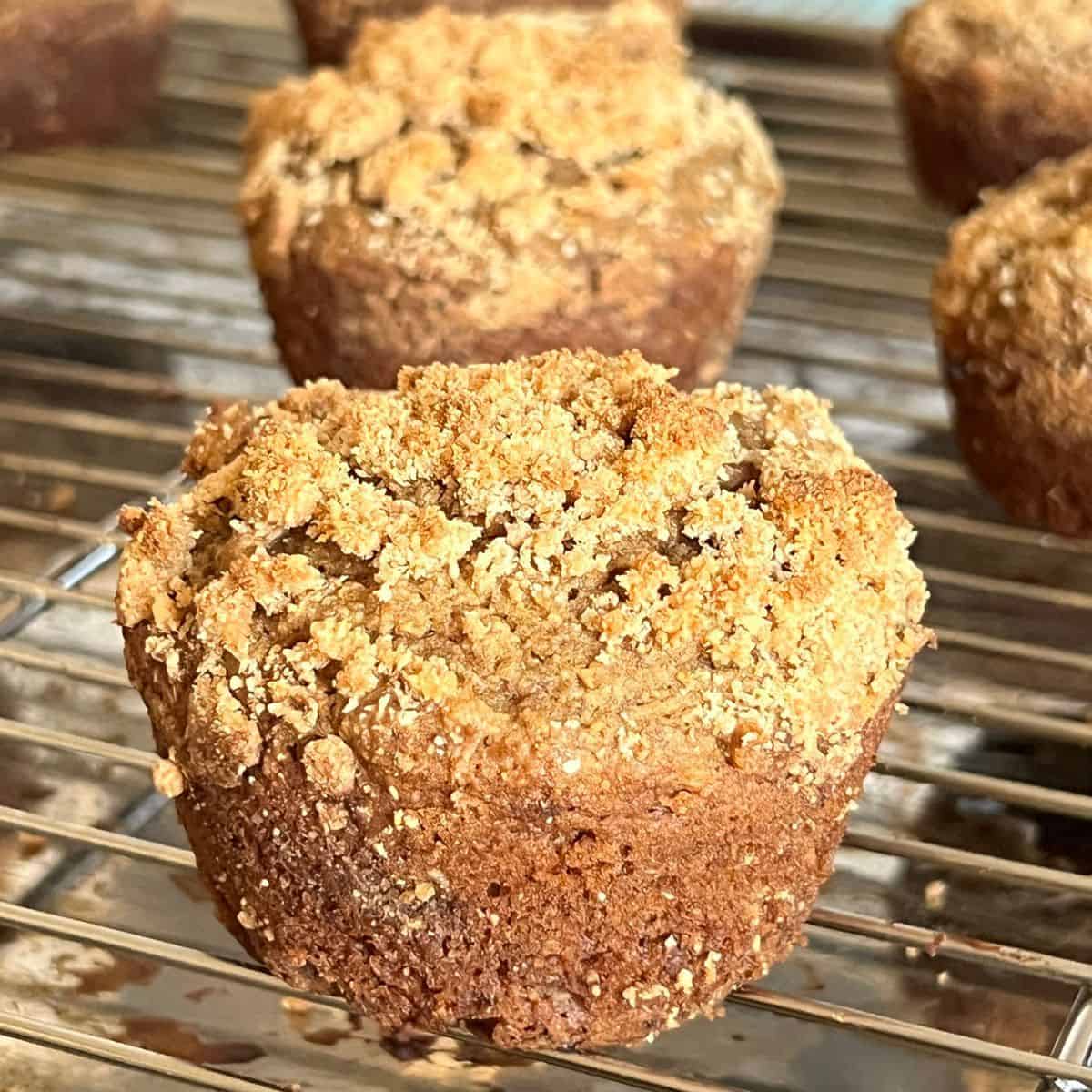 Close-up of a golden brown coffee cake muffin with crumb topping on a wire rack, showing a soft, moist texture and cinnamon streusel top