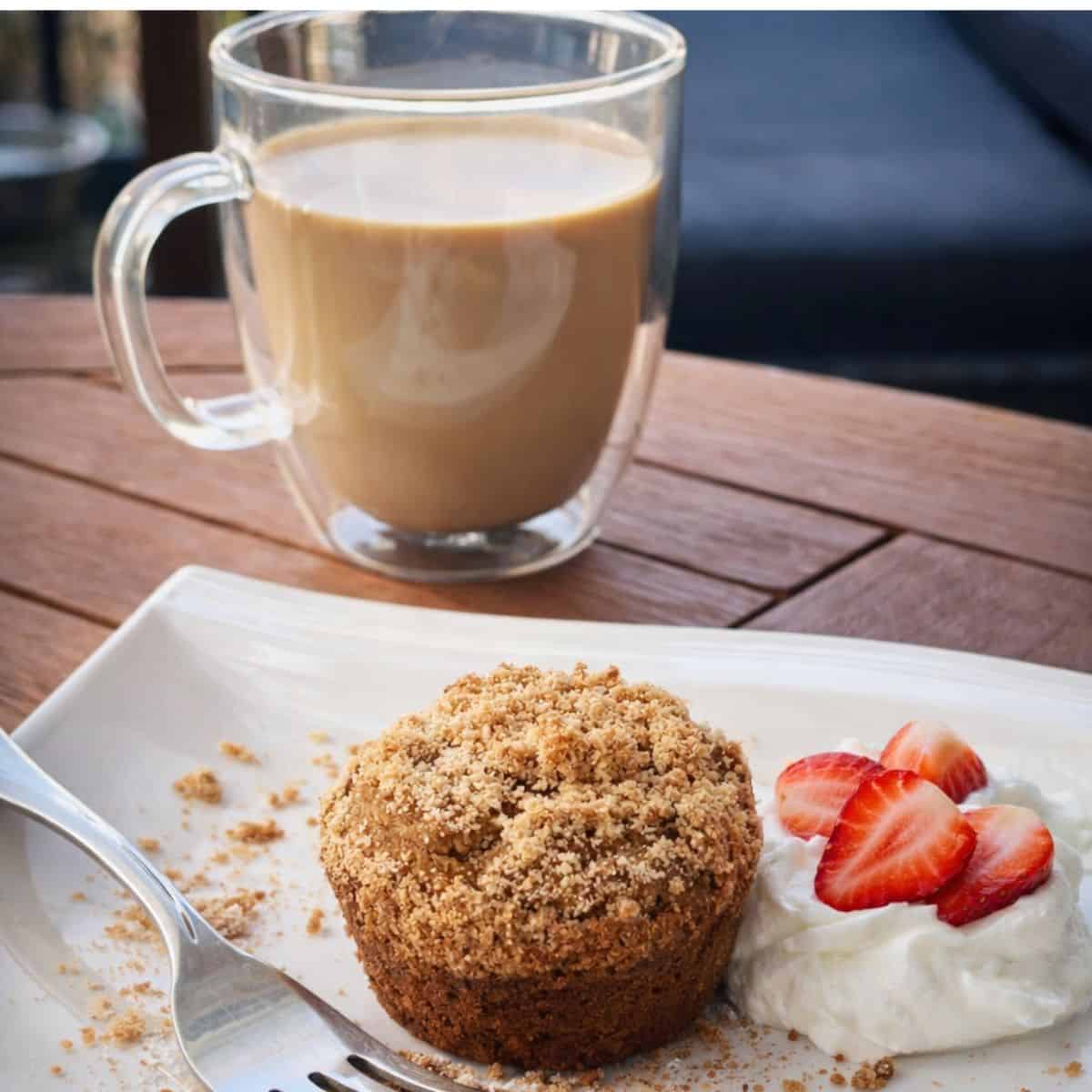 Greek yogurt coffee cake muffin with crumb topping served on a plate with yogurt and fresh strawberries, paired with a cup of coffee
