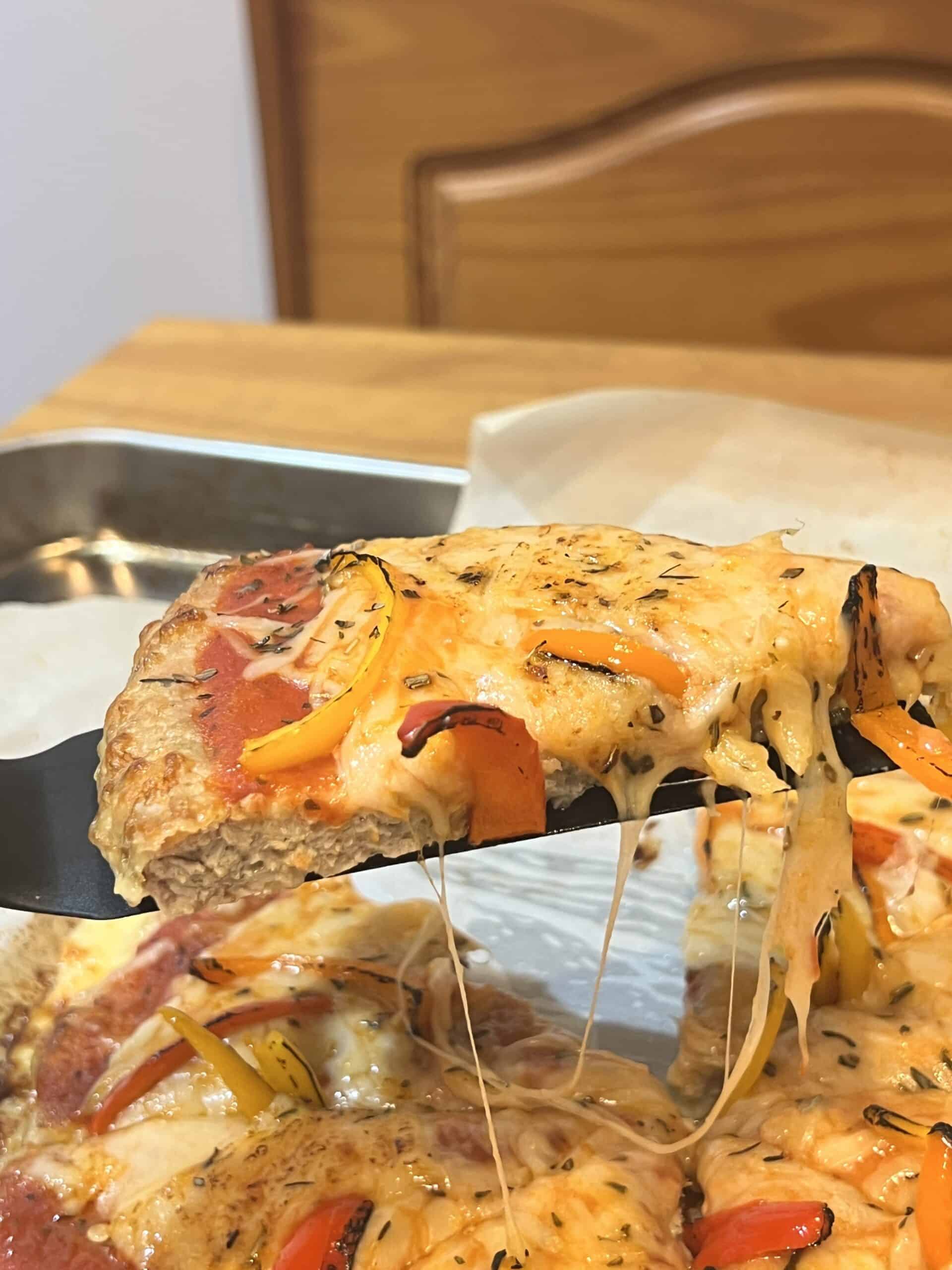 Slice of keto chicken crust pizza with melted cheese stretching, ready to serve